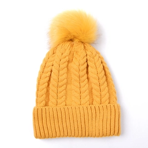 Détail de maille torsadée sur bonnet jaune avec pompon en fausse fourrure et bord côtelé