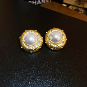 Macro shot of vintage gold-tone round pearl earrings with hammered texture and rhinestones