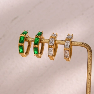 Bamboo style gold earrings with emerald and clear zircon crystals on marble display