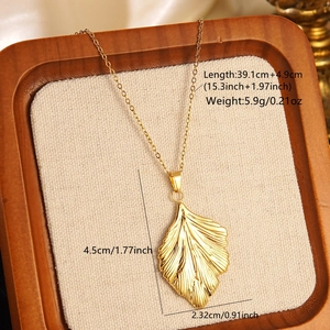 Detailed view of golden leaf pendant necklace with size measurements on wooden tray