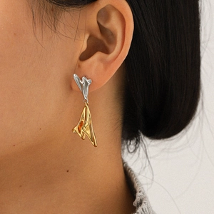 Detail shot of irregular two-tone gold and silver earrings on model ear with soft lighting