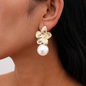 Close-up of golden flower pearl earrings with textured metal petals and sparkling center