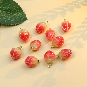 Close-up of handmade red strawberry charms with green leaves for DIY jewelry making