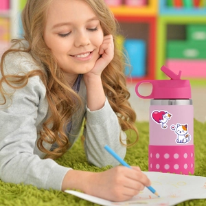 Pink kids insulated water bottle decorated with cute cartoon cat stickers on green carpet
