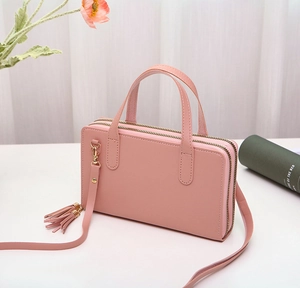 Pink faux leather crossbody bag with dual zipper compartments and decorative tassel