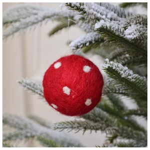 Macro detail of red wool felt Christmas ornament ball with white dots hanging on snowy branch