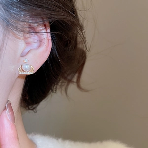Close-up of golden crown stud earring with white pearl and sparkling crystals on model