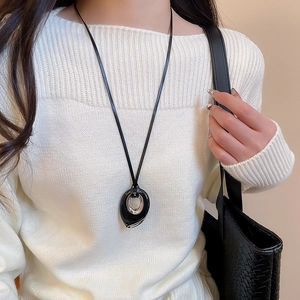Long leather necklace with black and silver oval pendant worn over white sweater