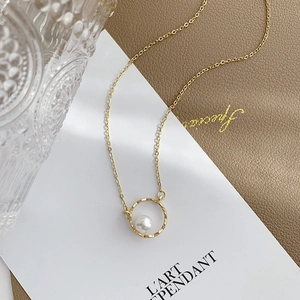 Geometric gold necklace with a round pearl pendant on a textured leather background