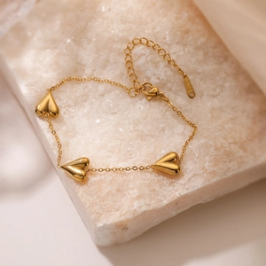 Gold plated stainless steel necklace featuring three heart pendants on a textured stone