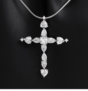 Détail du pendentif croix argentée avec zircons en forme de cœur et de poire sertis