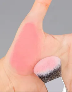Gros plan du pinceau biseauté estompant naturellement le blush sur la peau de la main