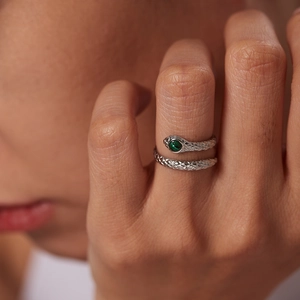 Detailed view of snake ring with green gemstone eyes and textured silver scales