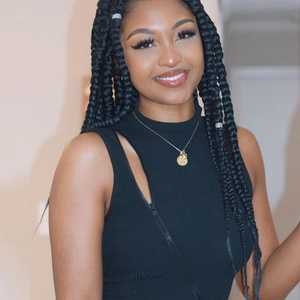 Détail de la robe noire sans manches à côtes avec collier doré pendentif R et cheveux tressés