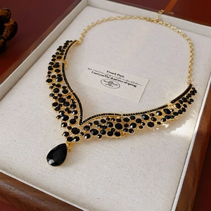 Detailed shot of a V-shaped gold necklace with black crystals in a wooden jewelry box