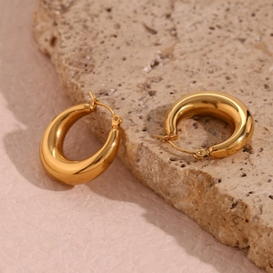 Detail shot of 18K gold plated thick hoop earrings on a textured beige stone background
