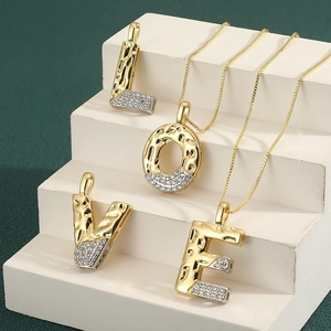 Two-tone gold and silver letter pendant necklaces with cubic zirconia on a white stand