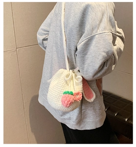 Detail view of a handmade white crochet bucket bag with pink strawberry and bunny ear accents