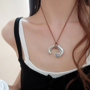 Detail of silver irregular C-shaped metal pendant on brown cord necklace worn by model