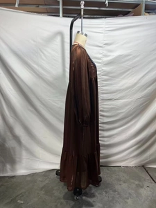 Détail d'une robe longue marron à manches longues avec tissu brillant et ourlet volanté