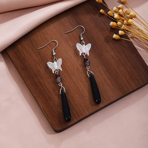 Close-up of butterfly drop earrings with black teardrop charms on a wooden surface