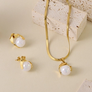 Gold stainless steel snake chain necklace and pearl stud earrings set on travertine stone