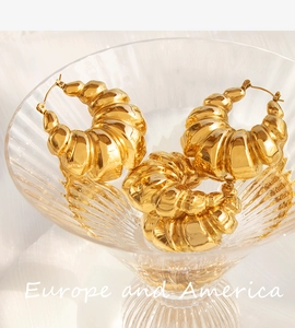 Artistic close-up of golden croissant style hoop earrings inside a textured glass cup