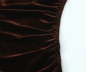 Gros plan sur la texture froncée et la broderie de la robe midi en velours marron foncé