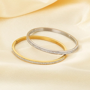 Dettaglio di bracciali ovali in oro 18k e argento con cristalli su seta champagne