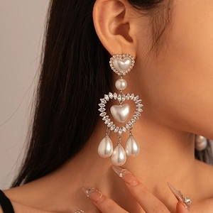 Close-up of heart-shaped pearl earrings with sparkling crystals and droplet pendants