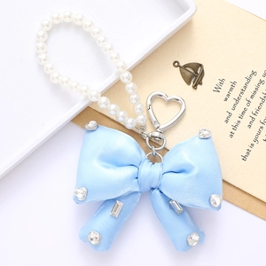 Detail of blue satin bow keychain with white pearls, rhinestones and silver heart ring