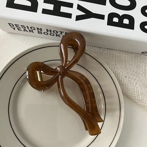 Macro detail of amber brown ribbon bow hair claw clip made of glossy acrylic with gold spring