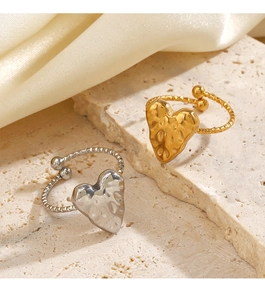 Dettaglio degli anelli a cuore martellato oro e argento su pietra con sfondo in seta beige