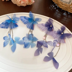 Detailed macro view of fabric butterfly earrings with crystal tassels on a ceramic plate