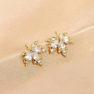 Détail macro de boucles d'oreilles feuille d'érable dorées avec zircons sur soie