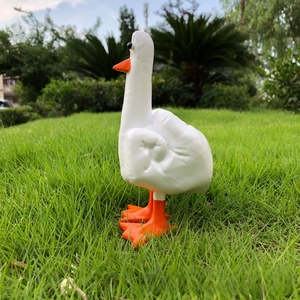 Detailed view of a white resin duck statue standing on a lawn in an outdoor garden