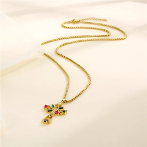 Golden cross necklace with colorful zircons on beige fabric background for women