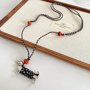 Close-up of ceramic dachshund pendant with black and white woven rope and red beads