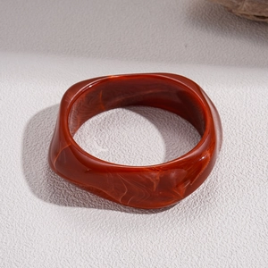 Macro shot of irregular wavy resin bangle with marbled amber red texture on white surface