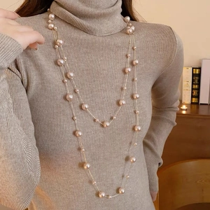 Détail d'un long collier de perles champagne à double rangée sur un col roulé beige