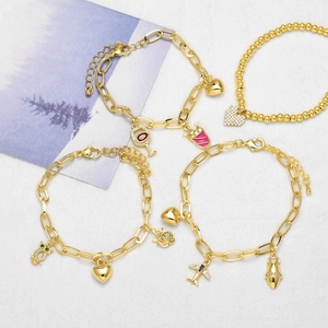 Set di bracciali a catena dorata con ciondoli cuore, aereo e calice su sfondo morbido