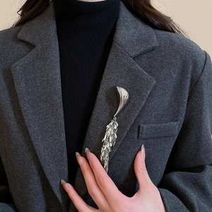 Detail of silver geometric brooch with leaf tassels on a dark grey tweed blazer