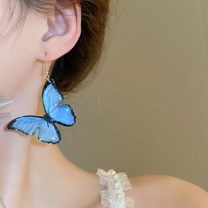 Close-up of elegant blue gradient butterfly earrings worn by a model on a beige background