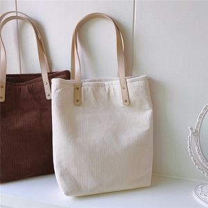Detail of corduroy tote bags in beige and brown with leather straps and metal rivets