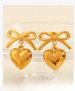 Detailed macro of gold-plated stainless steel bow and heart earrings on glass