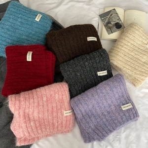 Close-up of soft knit wool scarves in multiple colors with woven labels on white fabric