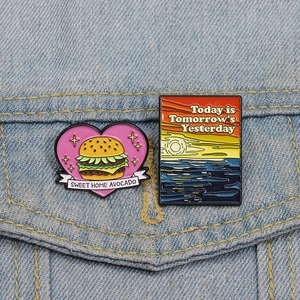 Artistic metal pins featuring a burger heart and sunset scenery on blue denim fabric