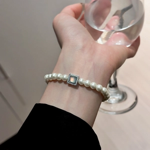 Detailed view of a French pearl bracelet with a square moonstone pendant on a wrist