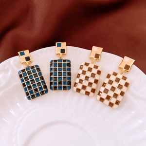 Detailed view of rectangular checkered enamel earrings on a white embossed porcelain plate