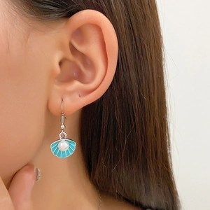 Close-up of blue enamel shell earrings with a white pearl on a model's ear
